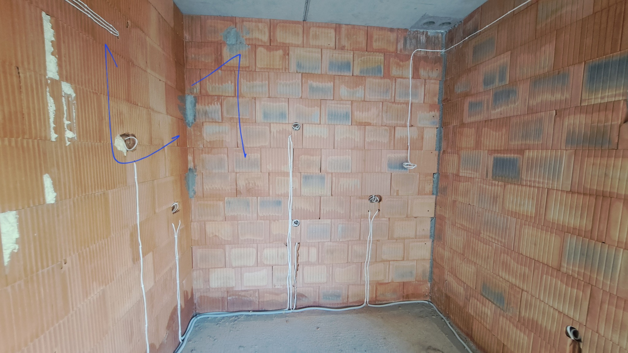 Surowa ściana z cegieł dziurawki w Katowicach z widocznymi przewodami elektrycznymi wychodzącymi z puszek instalacyjnych, przygotowana do dalszych prac wykończeniowych.