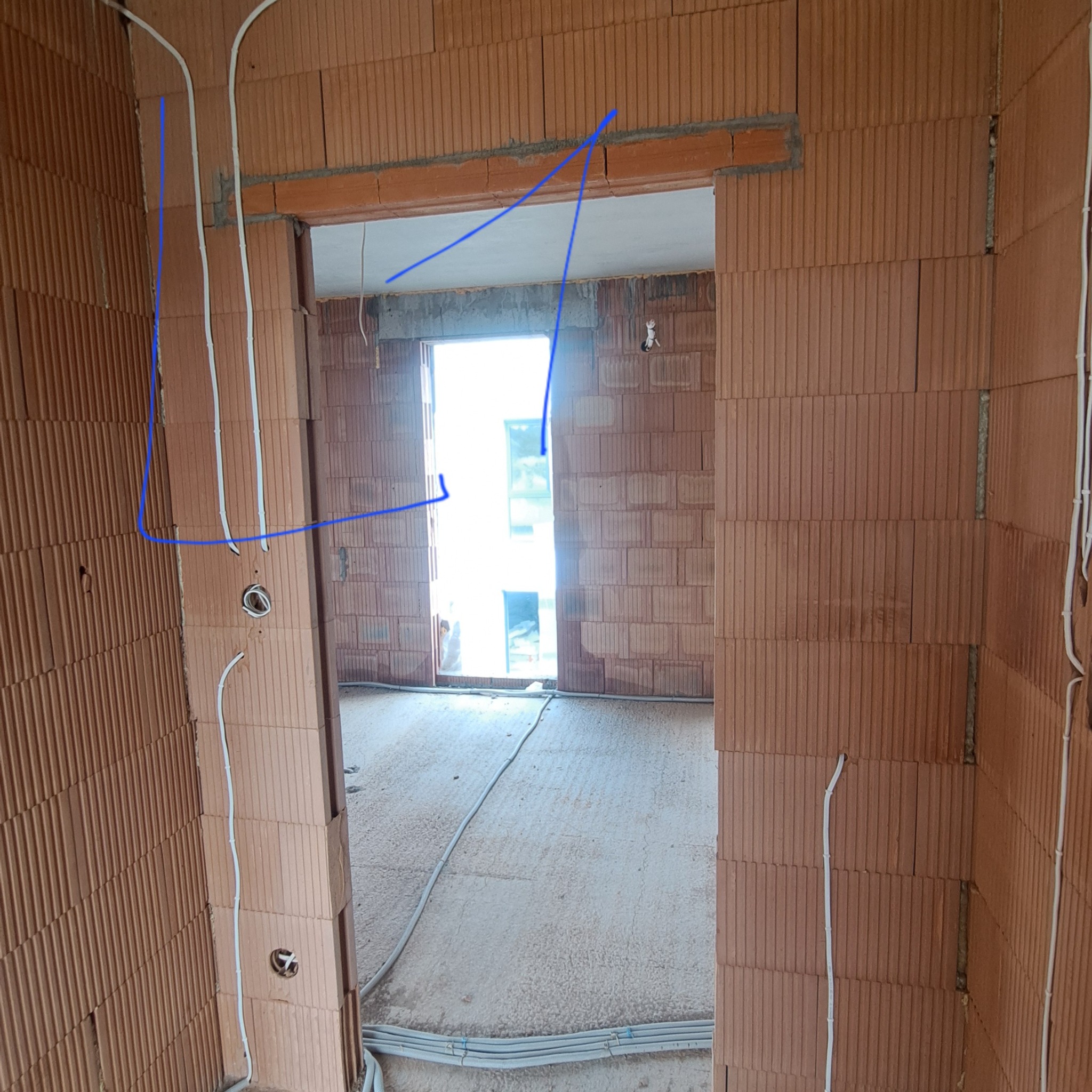 Wnętrze budynku w trakcie budowy z widocznymi przewodami elektrycznymi poprowadzonymi po ścianach z cegły ceramicznej, przygotowanymi do dalszych prac.