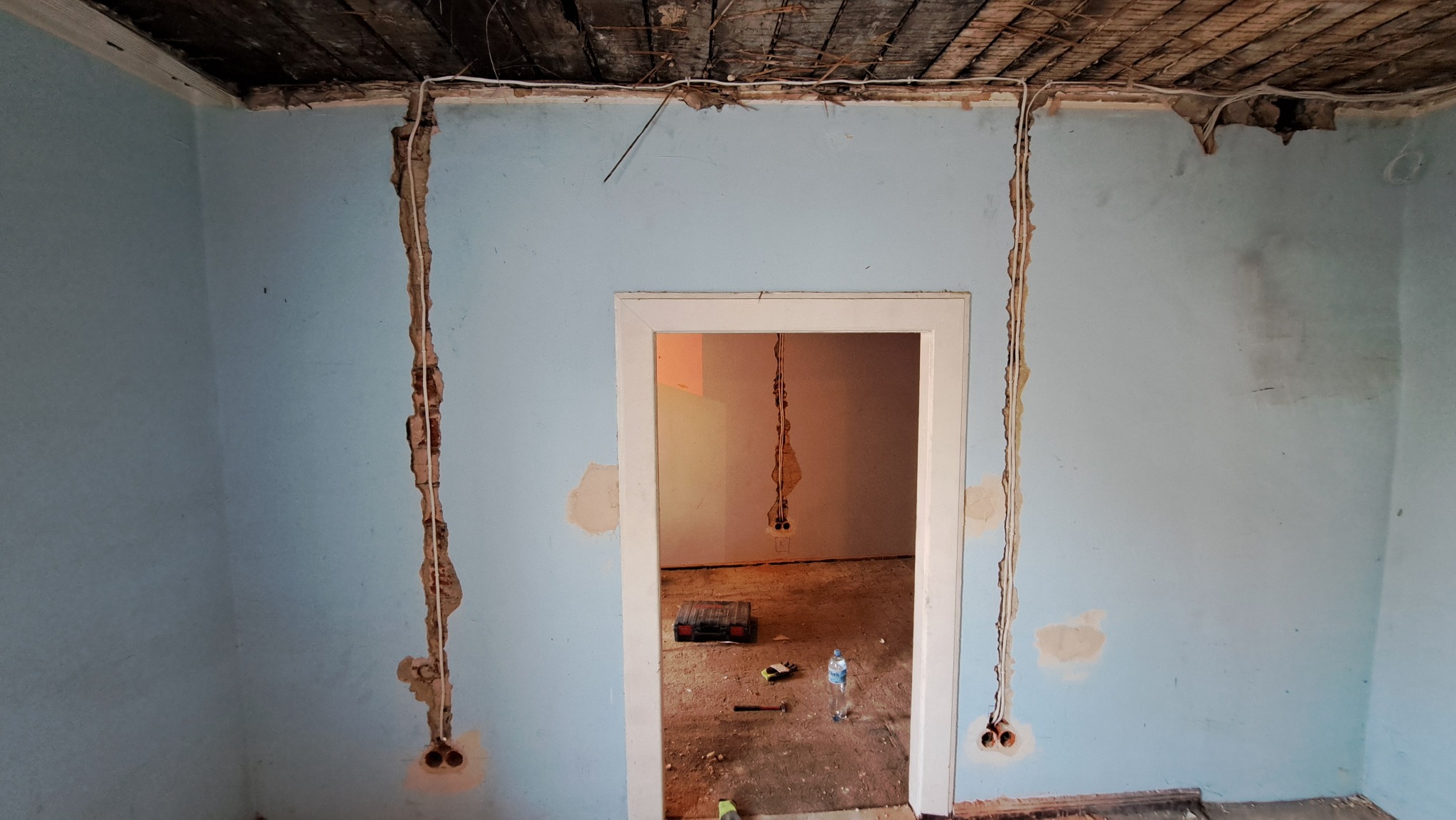 Przygotowanie do rozprowadzenia przewodów elektrycznych w starym domu: kable prowadzone w bruzdach wyciętych w ścianach, widoczne puszki instalacyjne, surowy strop z desek.