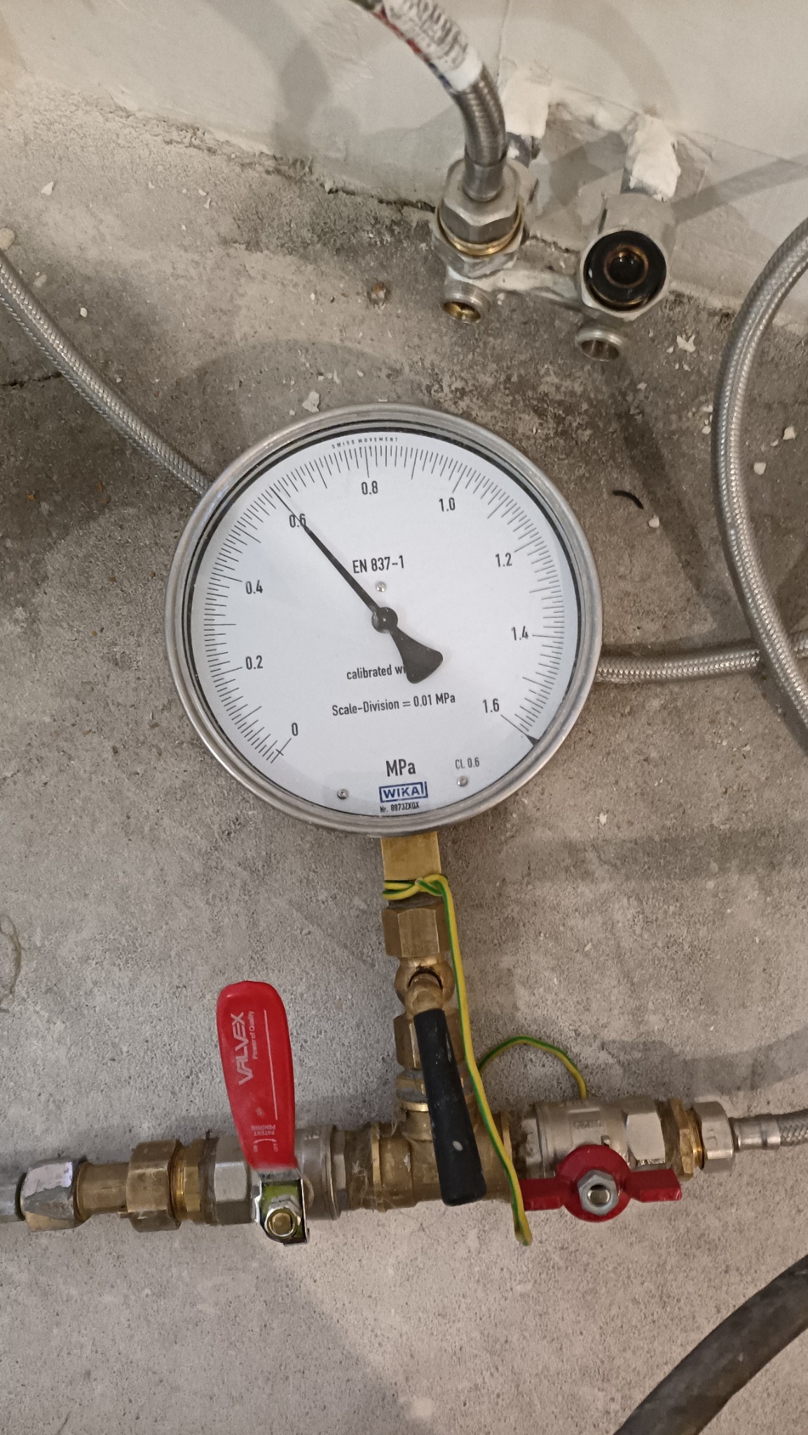 Manometr WIKA wskazujący ciśnienie w instalacji, widoczne zawory i elementy instalacji hydraulicznej na tle surowej ściany.