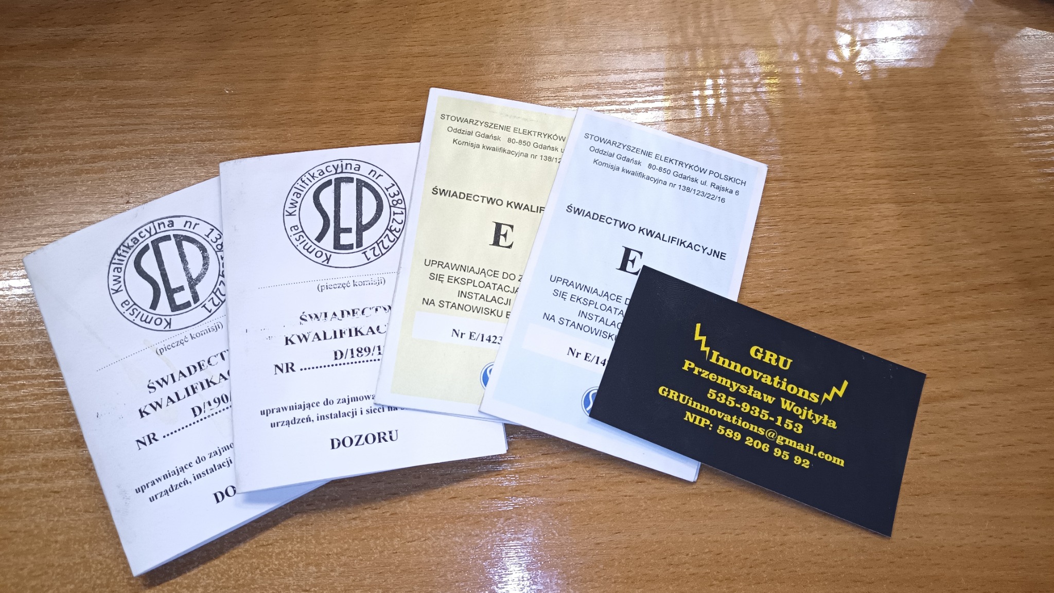 Zestaw dokumentów kwalifikacyjnych SEP i wizytówka firmy GRU Innovations na drewnianym blacie biurka.