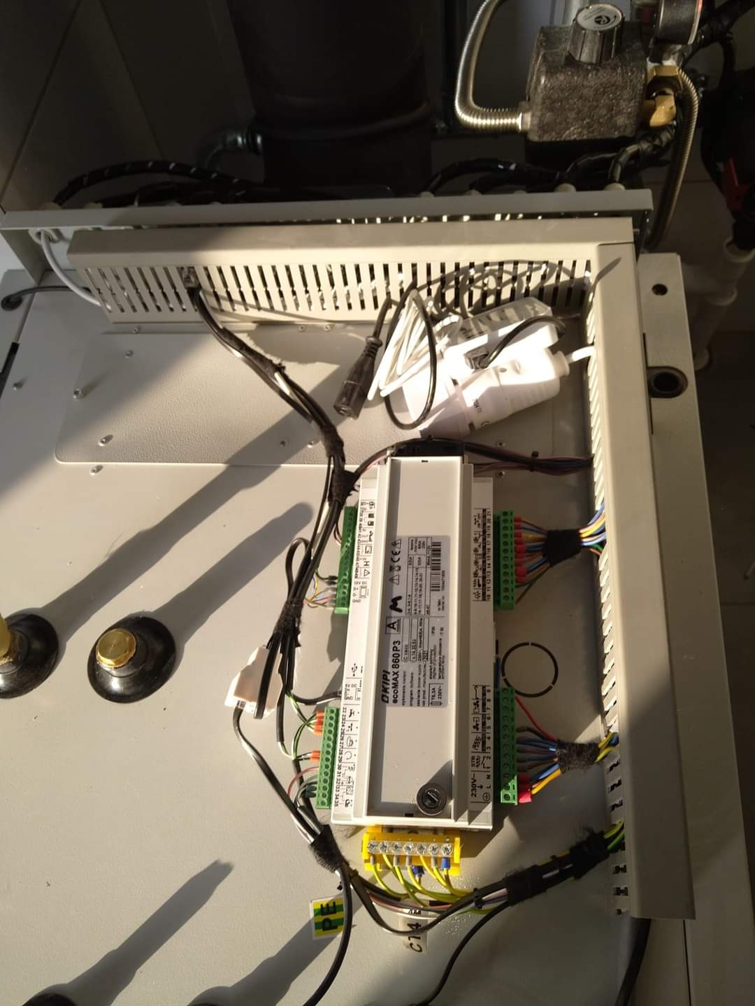 Wnętrze szafki sterowniczej z modułem OKIPI BIOCOMAX 860 P3, widoczne okablowanie, listwy zaciskowe i elementy instalacji grzewczej.