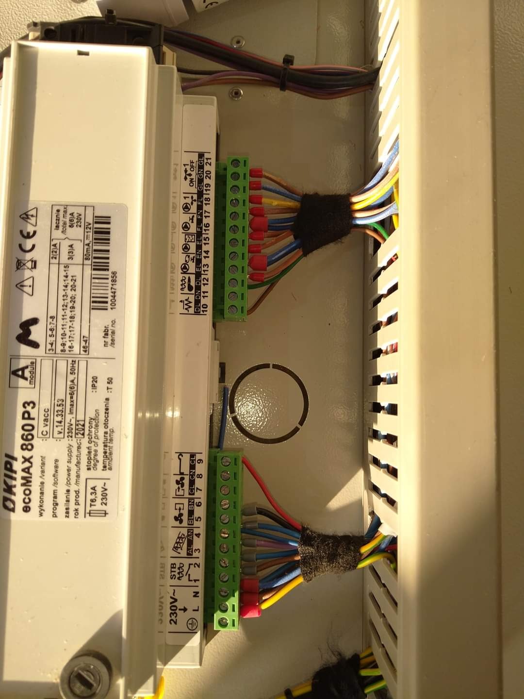 Panel sterowania kotłem grzewczym OKIPI ecoMAX 860 P3 z widocznymi kolorowymi przewodami podłączonymi do złączek, zabezpieczonymi czarną taśmą izolacyjną. Widoczne oznaczenia napięcia i prądu...