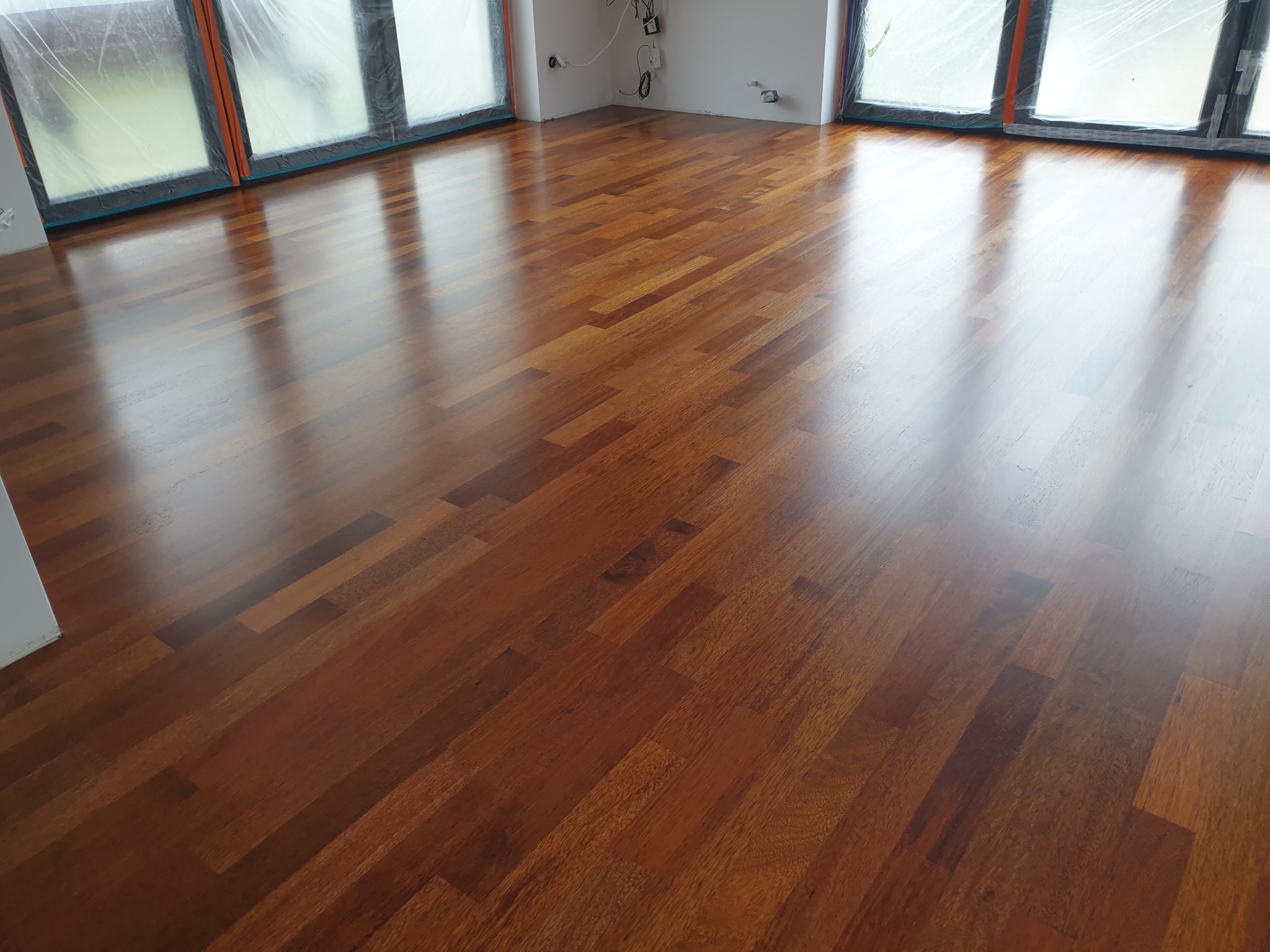 Nowo ułożony, lśniący parkiet z egzotycznego drewna w pustym pomieszczeniu z oknami zabezpieczonymi folią malarską.