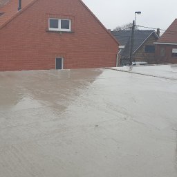 Investa - Świeżo wylany, mokry strop betonowy na budowie domu jednorodzinnego, widoczne rury instalacyjne zabezpieczone folią, w tle zabudowa mieszkalna.