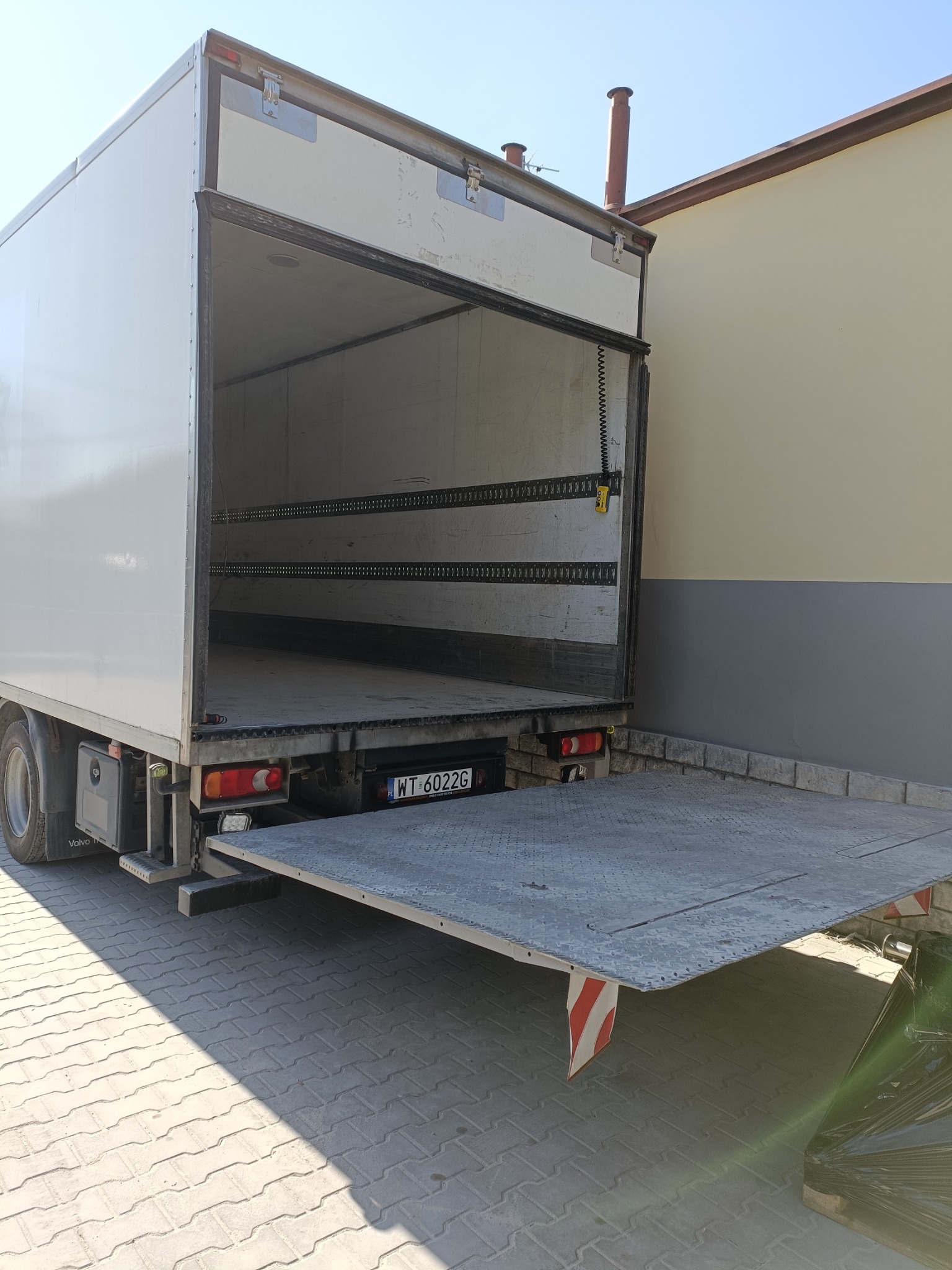 Otwarta pusta przestrzeń ładunkowa samochodu ciężarowego z windą załadowczą w Warszawie, widok z tyłu na zewnątrz.