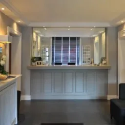 Recepcja w hotelu z oświetleniem punktowym, lustrami i kwiatami w wazonie.