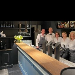 Meg@wat Jacek Remplakowski - Zespół barmanów i kelnerów w eleganckim lokalu z czarnymi elementami wystroju, widoczne dystrybutory do piwa i półki z alkoholem.