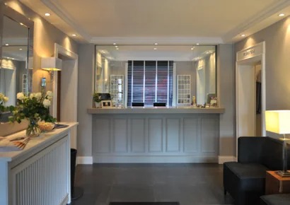 Recepcja w hotelu z oświetleniem punktowym, lustrami i kwiatami w wazonie.