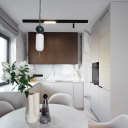 OYAA - Nowoczesna, minimalistyczna kuchnia z marmurowym akcentem, okrągłym stołem z bukietem białych lilii i designerską lampą wiszącą z elementami marmuru.
