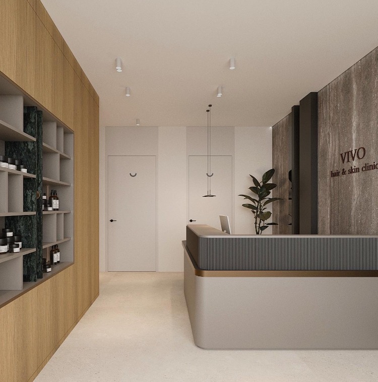 Nowoczesne wnętrze recepcji salonu kosmetycznego VIVO z minimalistycznym biurkiem recepcyjnym, drewnianą zabudową z półkami na kosmetyki i ścianą z logo firmy.