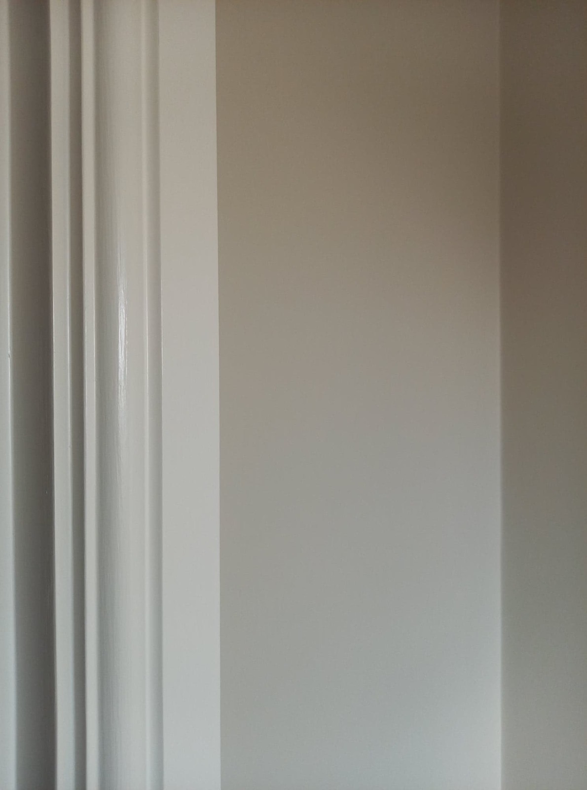 Ściana pomalowana na dwa odcienie beżu, z widocznymi pionowymi listwami dekoracyjnymi w jaśniejszym odcieniu, tworzącymi minimalistyczny wzór.