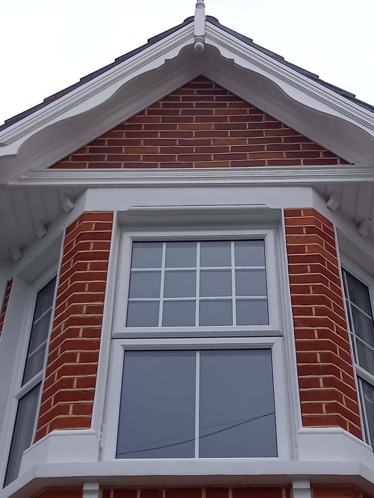 Fragment elewacji domu z cegły klinkierowej z białymi, ozdobnymi elementami architektonicznymi i nowymi oknami PCV z białymi szprosami, widok z dołu.