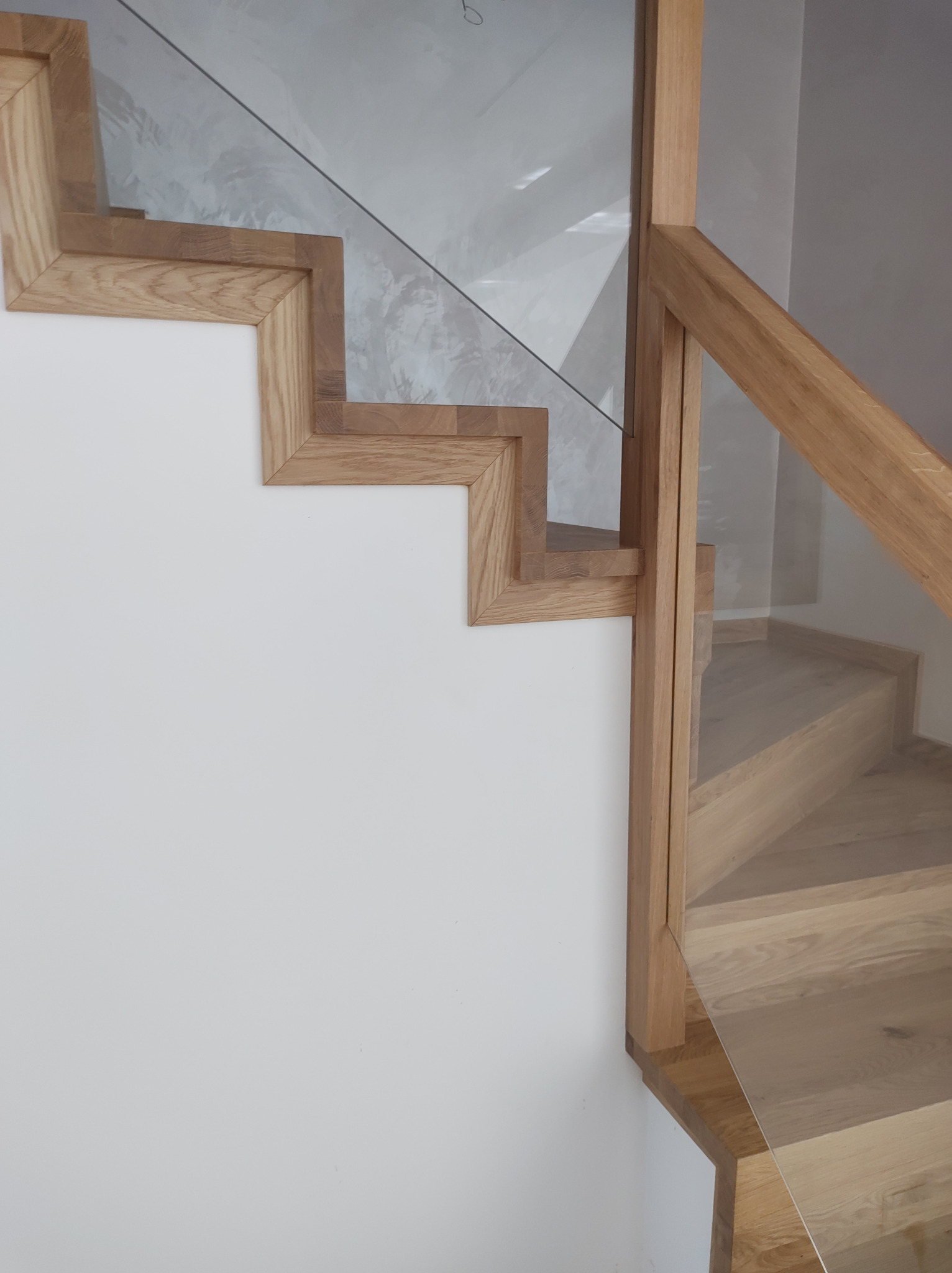 Detale drewnianych schodów z jasnego drewna z szklaną balustradą, widok z dołu, podkreślający geometryczny kształt stopni i minimalistyczny design.