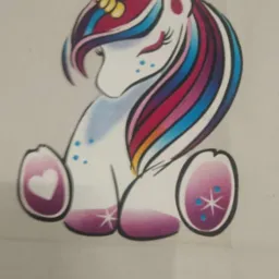 Grafika przedstawia uroczego jednorożca z kolorową grzywą i ogonem w odcieniach różu, fioletu i błękitu, siedzącego na tylnych nogach z gwiazdkami i trzymającego przed sobą dwa jajka z sercem...