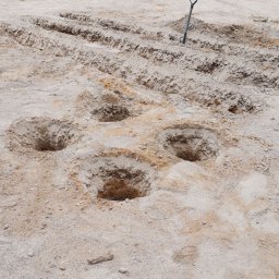 ARCHEMI Sp. z o.o. - Przygotowanie terenu pod plac zabaw: wykopane doły, mini koparka i pracownik w tle.