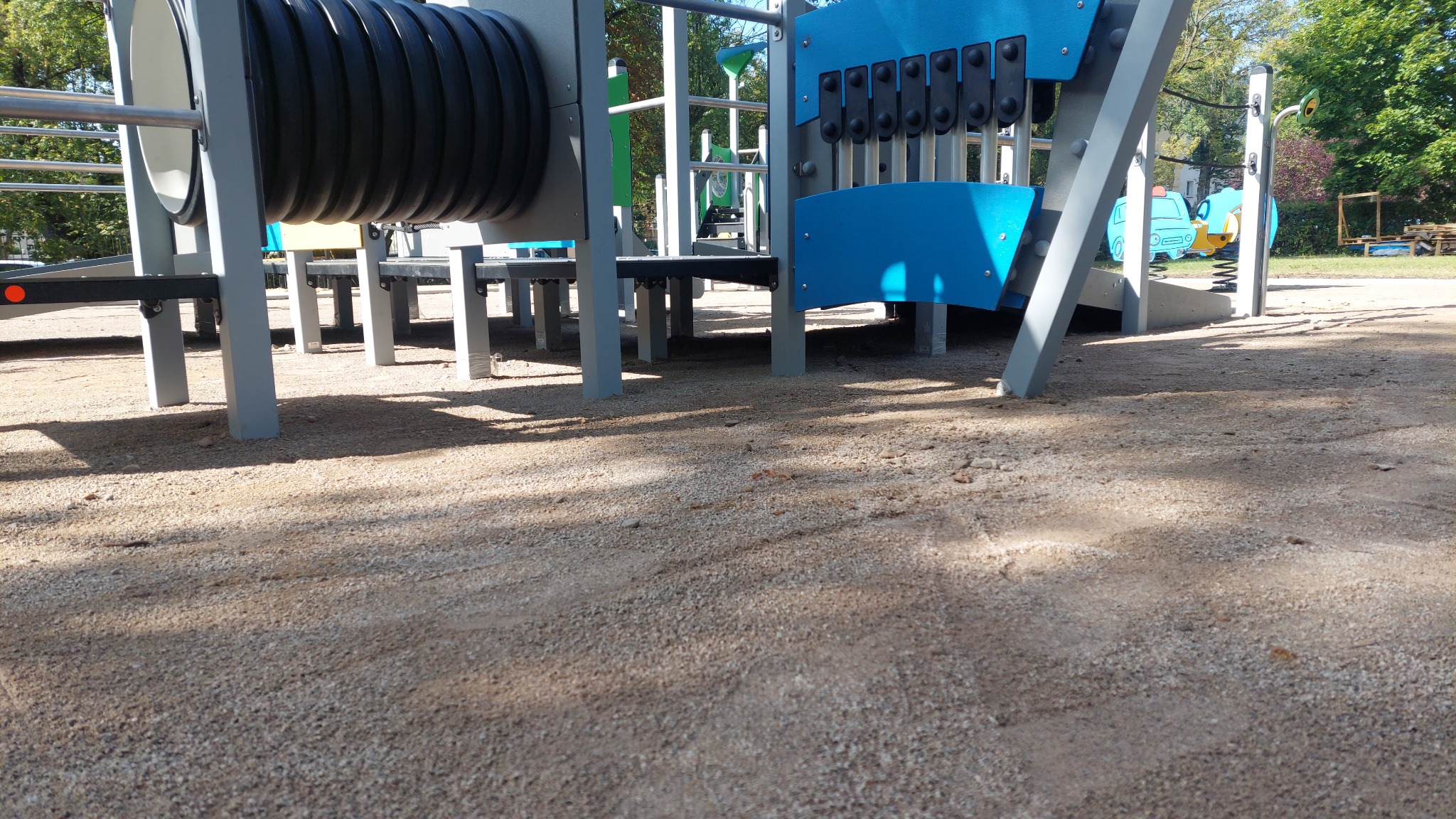 Fragment konstrukcji placu zabaw w Turku, z tunelem i elementami interaktywnymi, widziany z perspektywy gruntu pokrytego drobnym żwirem.