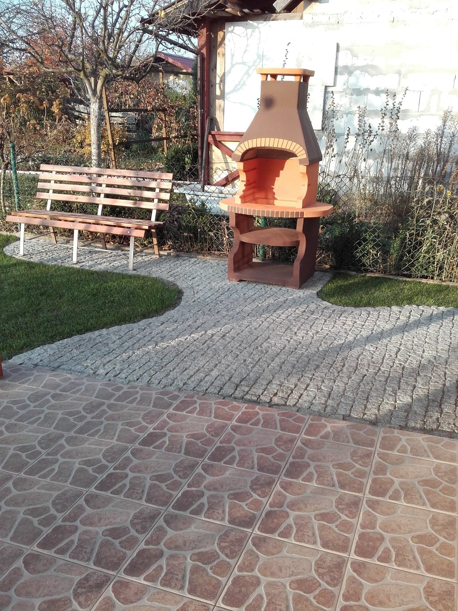 Ułożona ścieżka z kostki granitowej we Wrocławiu, prowadząca od tarasu z płytek ceramicznych do grilla ogrodowego i ławki w ogrodzie.