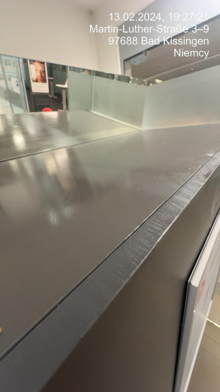 Błyszczący, szary blat biurka z widocznymi refleksami światła, z datą i adresem naniesionymi na zdjęcie, prawdopodobnie zrobione po czyszczeniu.