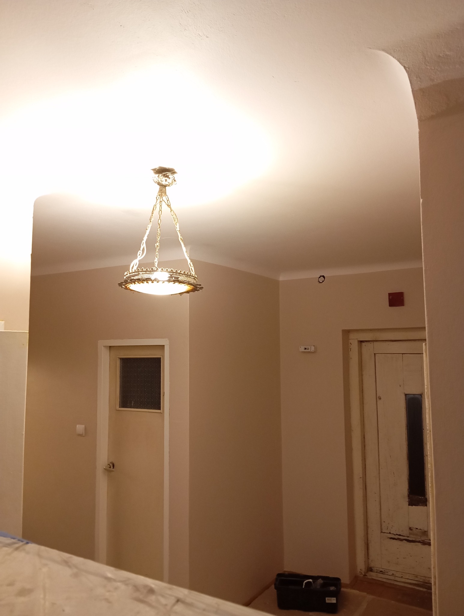 Wnętrze po odświeżeniu koloru ścian, z widocznym ozdobnym żyrandolem, dwoma parami drzwi i skrzynką z narzędziami na podłodze.