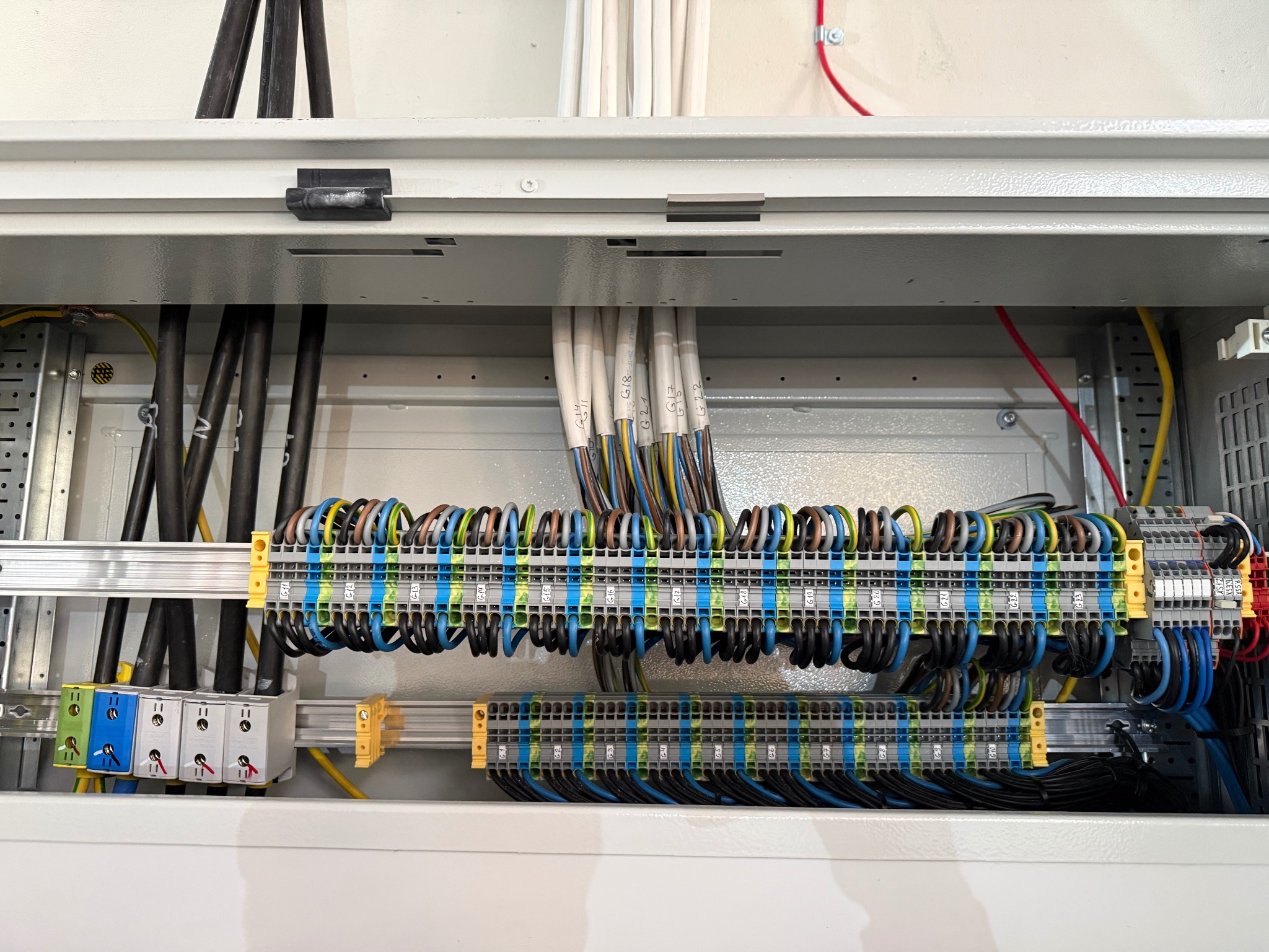 Rozdzielnica elektryczna z precyzyjnie ułożonymi przewodami oznaczonymi numerami, widoczne listwy zaciskowe i kable w kolorowej izolacji. Estetyczny montaż w szarej obudowie.