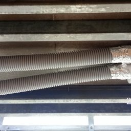 JP TANI DOM SPÓŁKA Z OGRANICZONĄ ODPOWIEDZIALNOŚCIĄ - Dwa elastyczne przewody wentylacyjne przymocowane do sufitu za pomocą metalowych wsporników i połączone z białym elementem wentylacyjnym, zabezpieczone folią aluminiową.