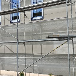 JP TANI DOM SPÓŁKA Z OGRANICZONĄ ODPOWIEDZIALNOŚCIĄ - Dom w trakcie kompleksowego ocieplania, widoczne rusztowania i płyty izolacyjne na elewacji, okna z czarną ramą.