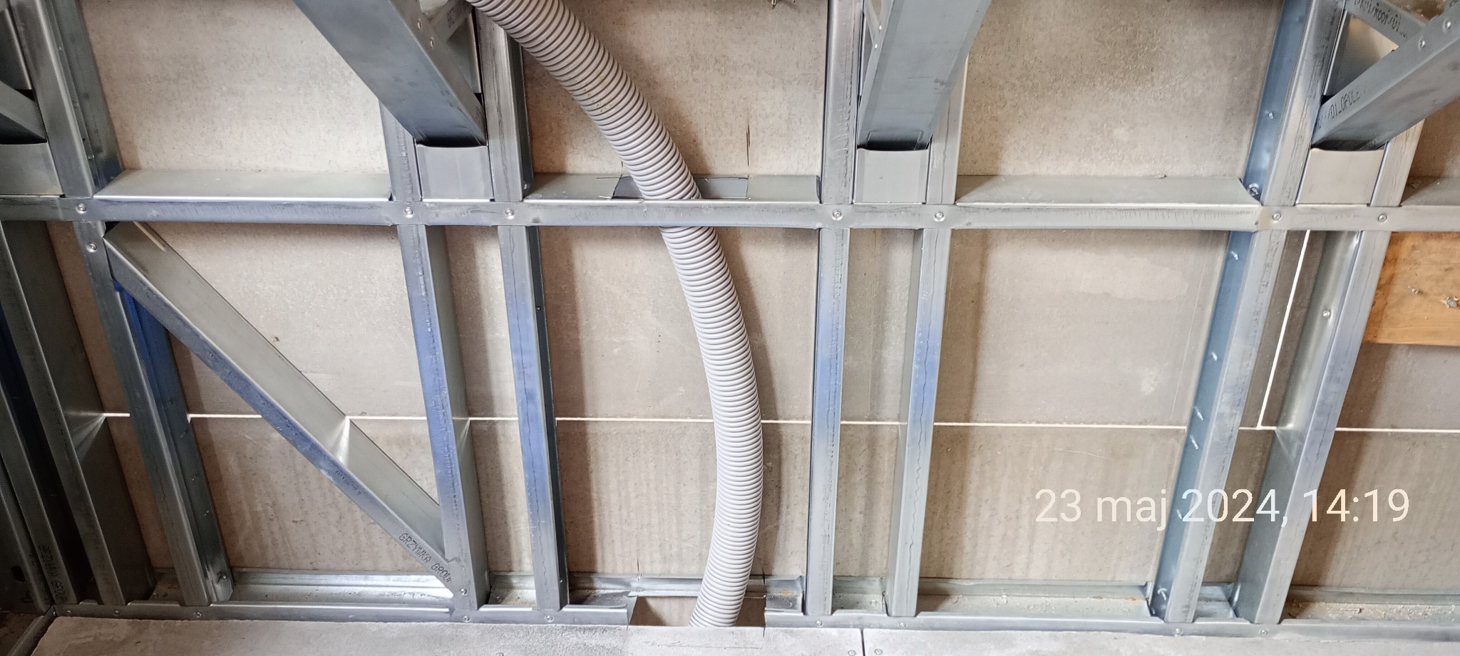 Konstrukcja szkieletowa ściany z metalowych profili z widoczną rurą instalacyjną wewnątrz, widok z dołu.