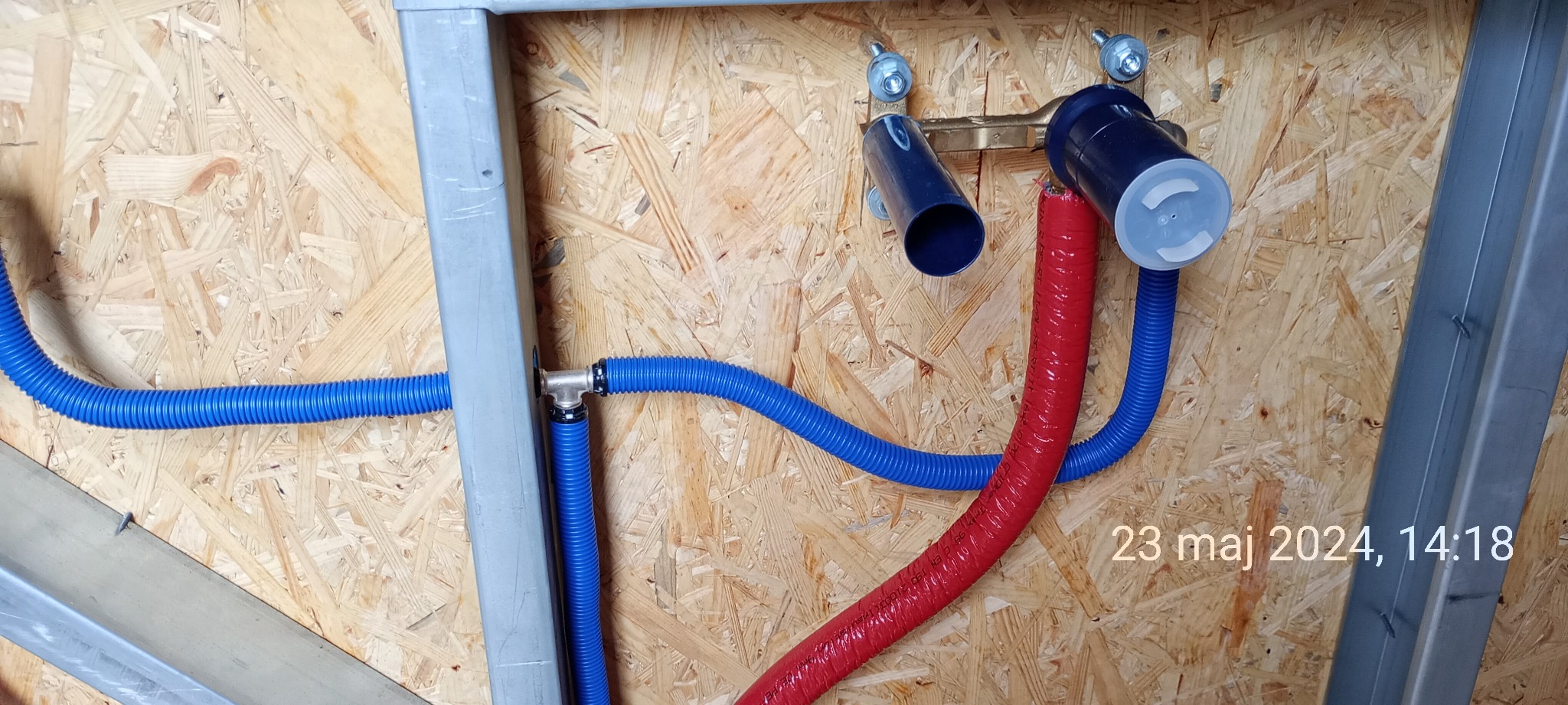 Instalacja wodna z niebieskich i czerwonych rur karbowanych przymocowana do płyty OSB w konstrukcji szkieletowej, widoczne metalowe profile i złączki.