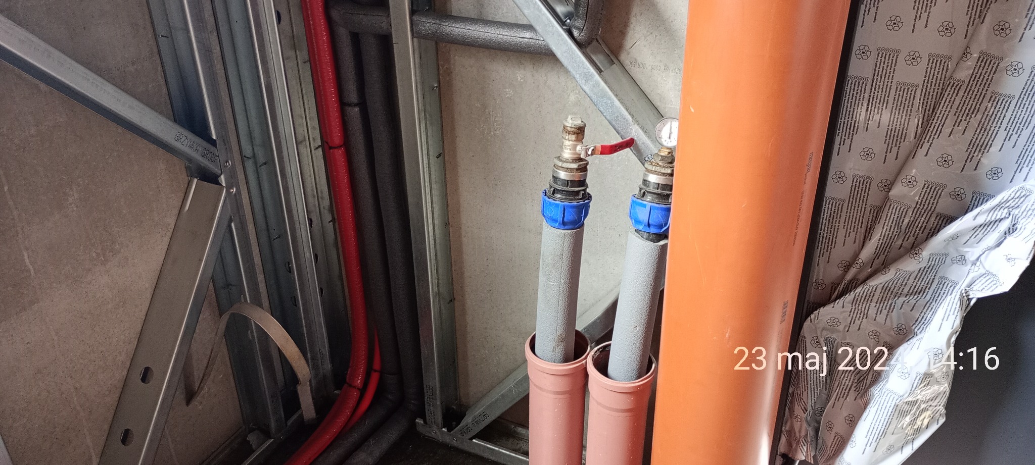 Instalacja wodna wewnątrz konstrukcji szkieletowej z widocznymi rurami, zaworami, manometrem i izolacją, w trakcie prac wykończeniowych z widoczną datą wykonania zdjęcia.