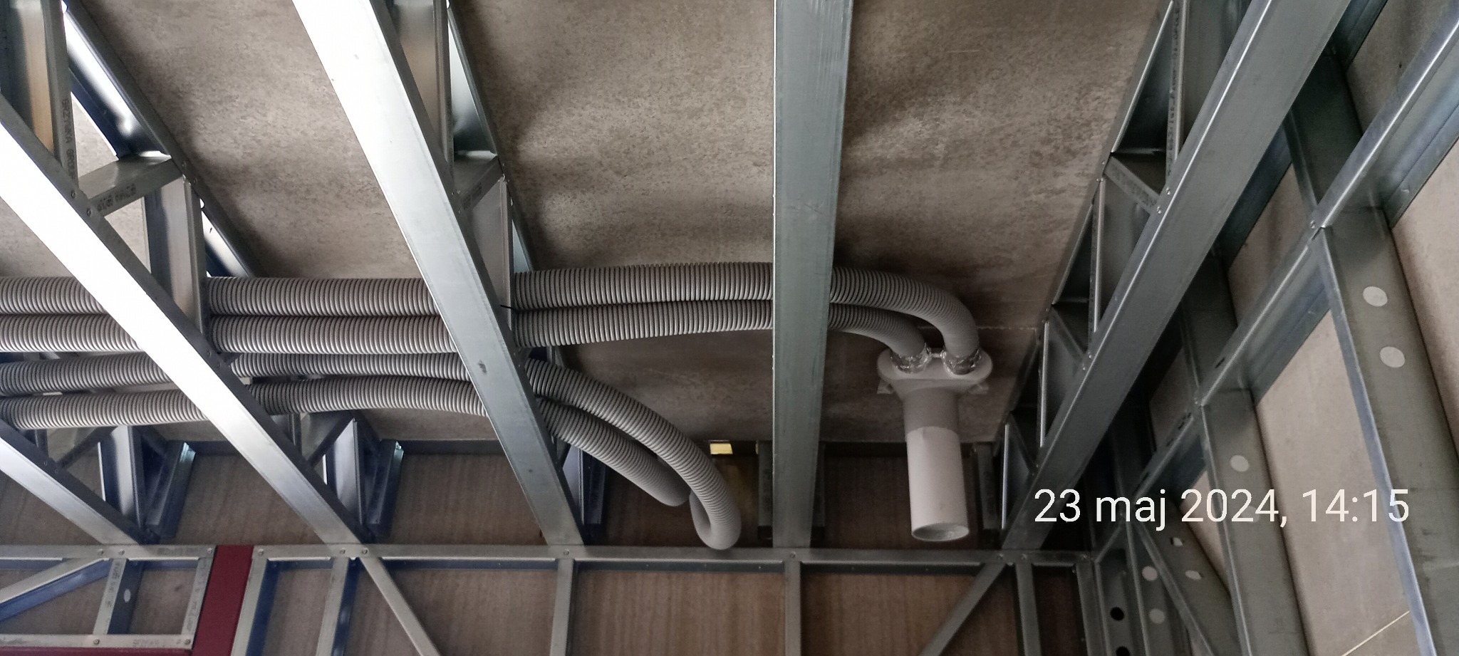 Metalowy szkielet konstrukcyjny budynku z widocznymi rurami instalacji wentylacyjnej pod stropem, widok z dołu.