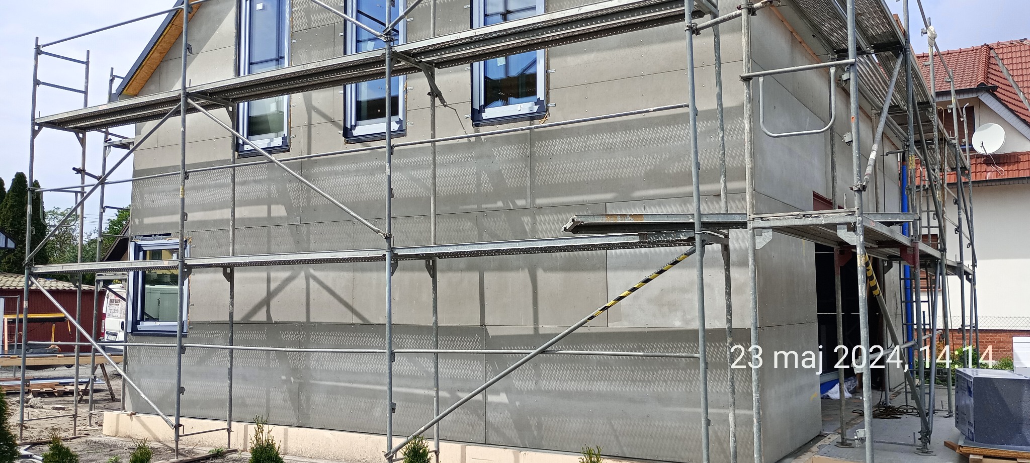 Dom w trakcie kompleksowego ocieplania, widoczne rusztowania i płyty izolacyjne na elewacji, okna z czarną ramą.