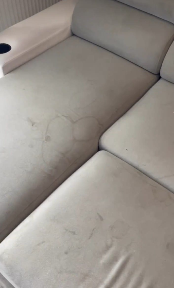 Jasna kanapa z widocznymi plamami przed czyszczeniem, z uchwytem na napoje po lewej stronie.