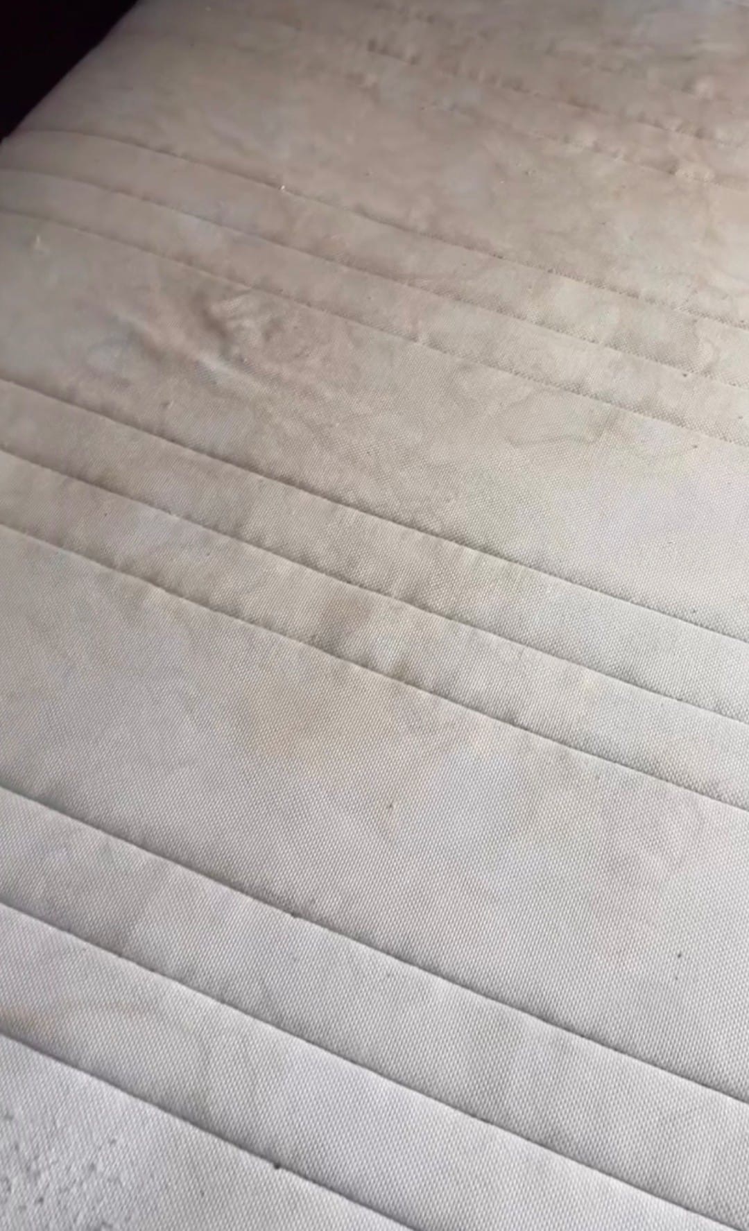 Widok z bliska na zabrudzony, jasny materac z wyraźnymi śladami plam i smug na powierzchni.