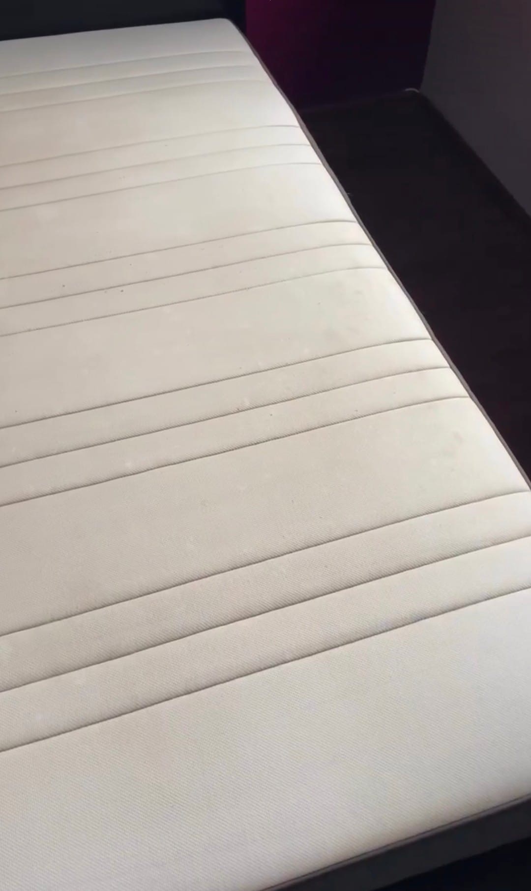 Beżowy materac łóżka z widocznymi plamami i śladami użytkowania, sfotografowany pod kątem.