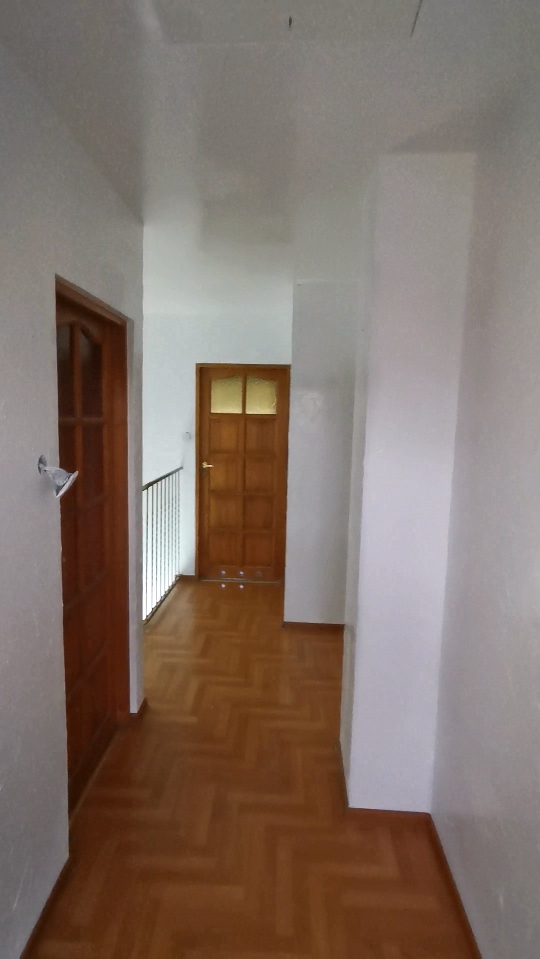 Korytarz po malowaniu z parkietem w jodełkę i dwiema drewnianymi drzwiami, widoczne niedoskonałości malowania sufitu.