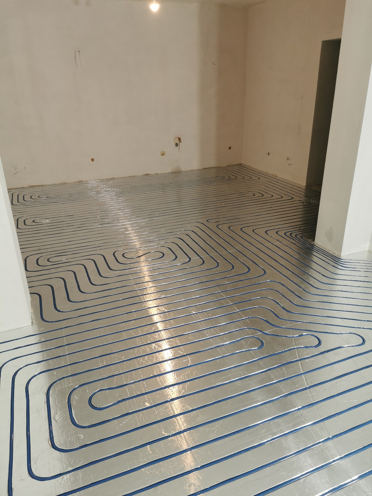 Instalacja ogrzewania podłogowego w Cieszynie, widoczne rury grzewcze ułożone na srebrnej folii izolacyjnej w surowym wnętrzu, przed wylaniem wylewki.