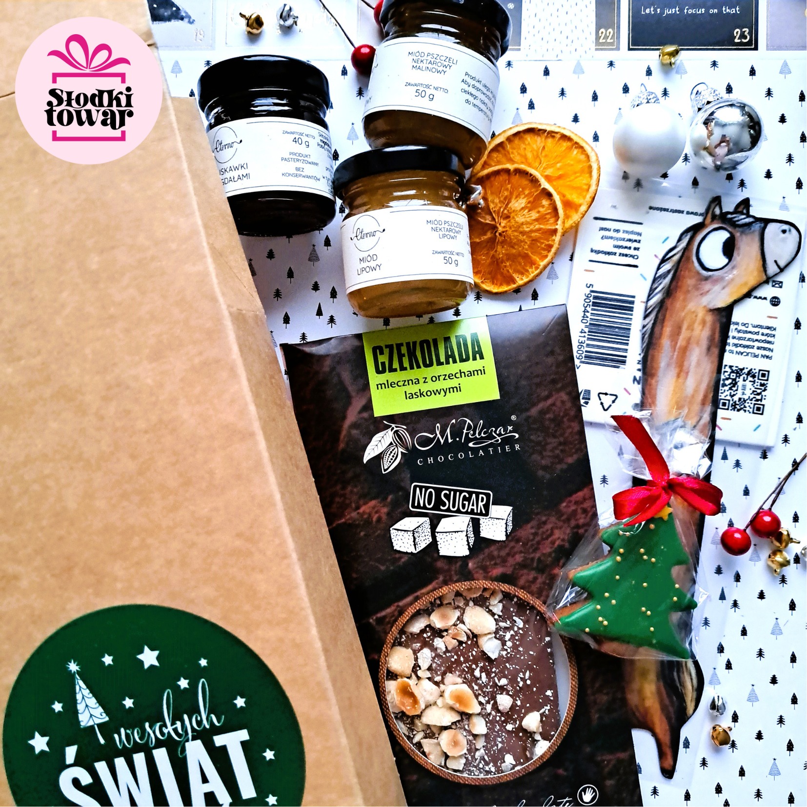 Zestaw prezentowy z miodami smakowymi, czekoladą bez cukru z orzechami laskowymi, piernikiem w kształcie choinki z kokardką i ozdobami świątecznymi, umieszczony w tekturowym pudełku z naklejką...