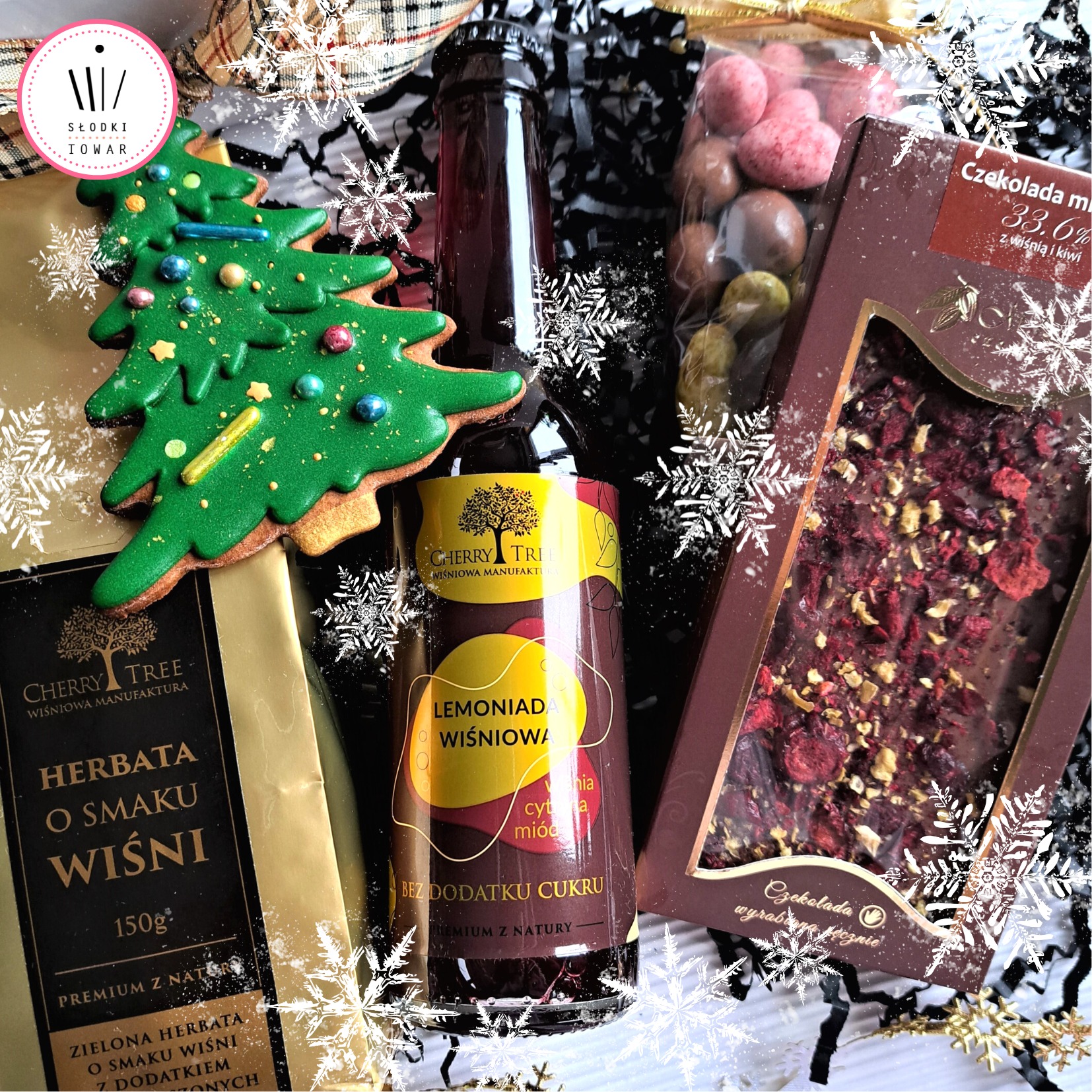 Świąteczny zestaw upominkowy z herbatą wiśniową, lemoniadą wiśniową, czekoladą z wiśnią i kiwi oraz piernikiem w kształcie choinki, zapakowany w ozdobny kosz.