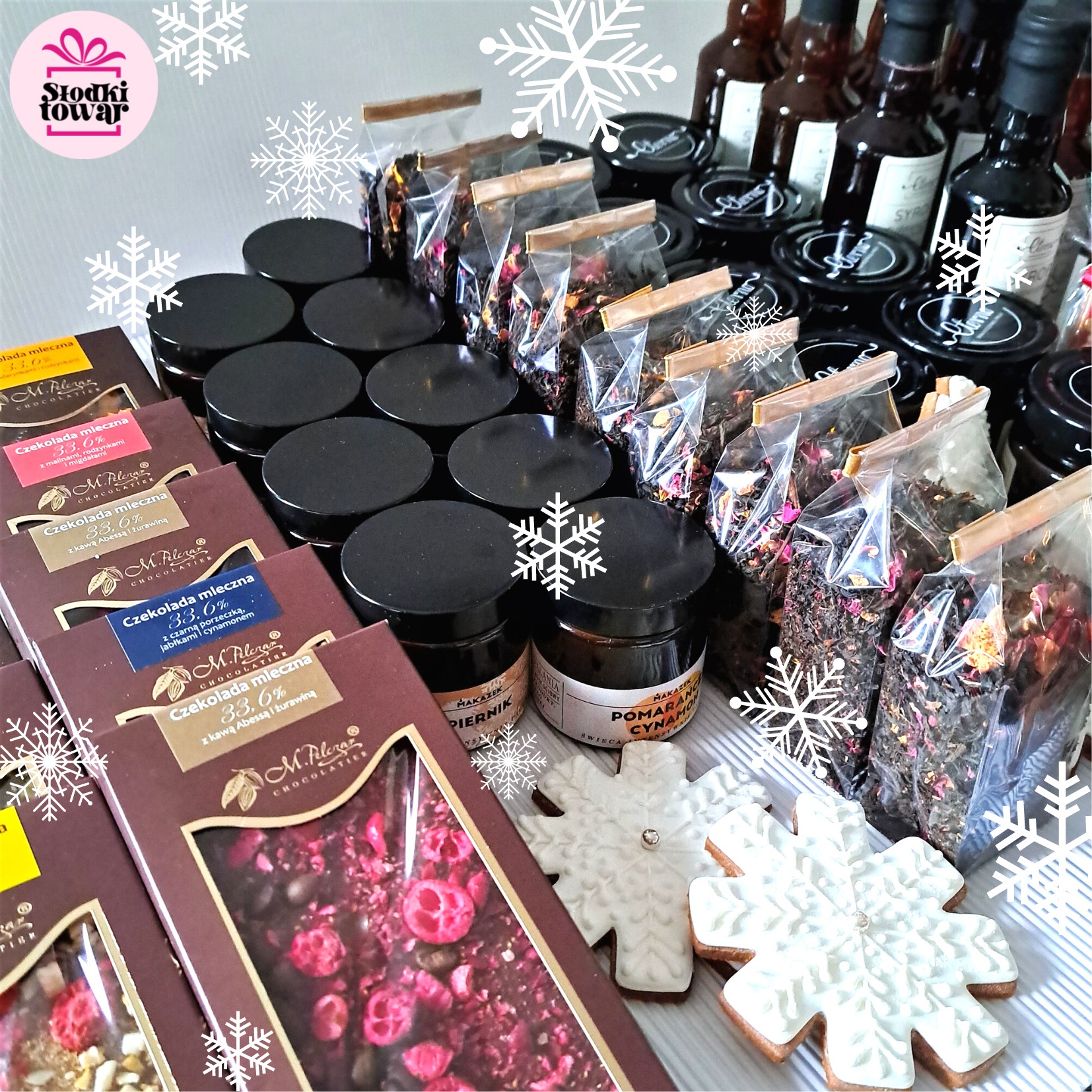 Zestaw upominkowy z czekoladami smakowymi, słoiczkami z przyprawami, herbatami w przezroczystych torebkach i pierniczkami w kształcie śnieżynek, całość w zimowej aranżacji.