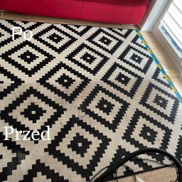 Michał Podolski - Dywan w geometryczne wzory, widoczna różnica w czystości: część 'po' jest wyraźnie jaśniejsza od części 'przed', widoczne urządzenie czyszczące w rogu.