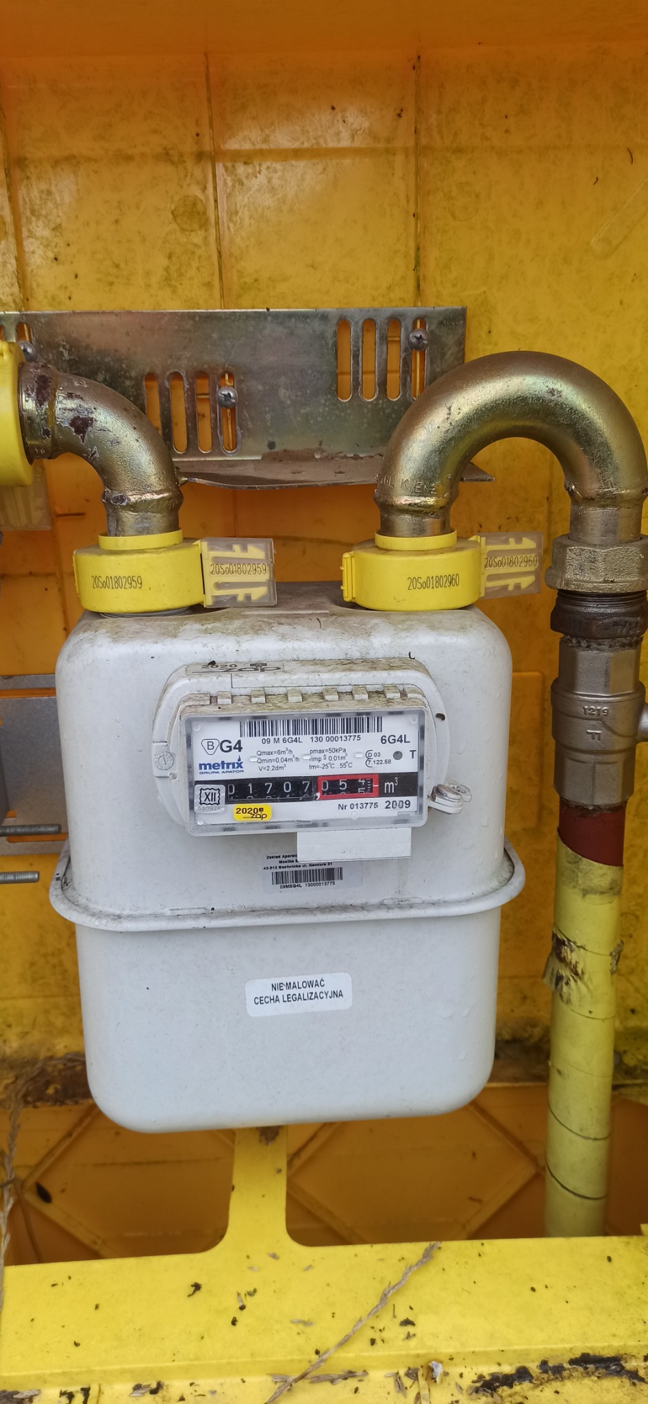 Gazomierz w żółtej obudowie, widoczne rury doprowadzające gaz z żółtymi zabezpieczeniami, stan licznika 01707.05 m3, cecha legalizacyjna 2009, naklejka 'Nie malować'.