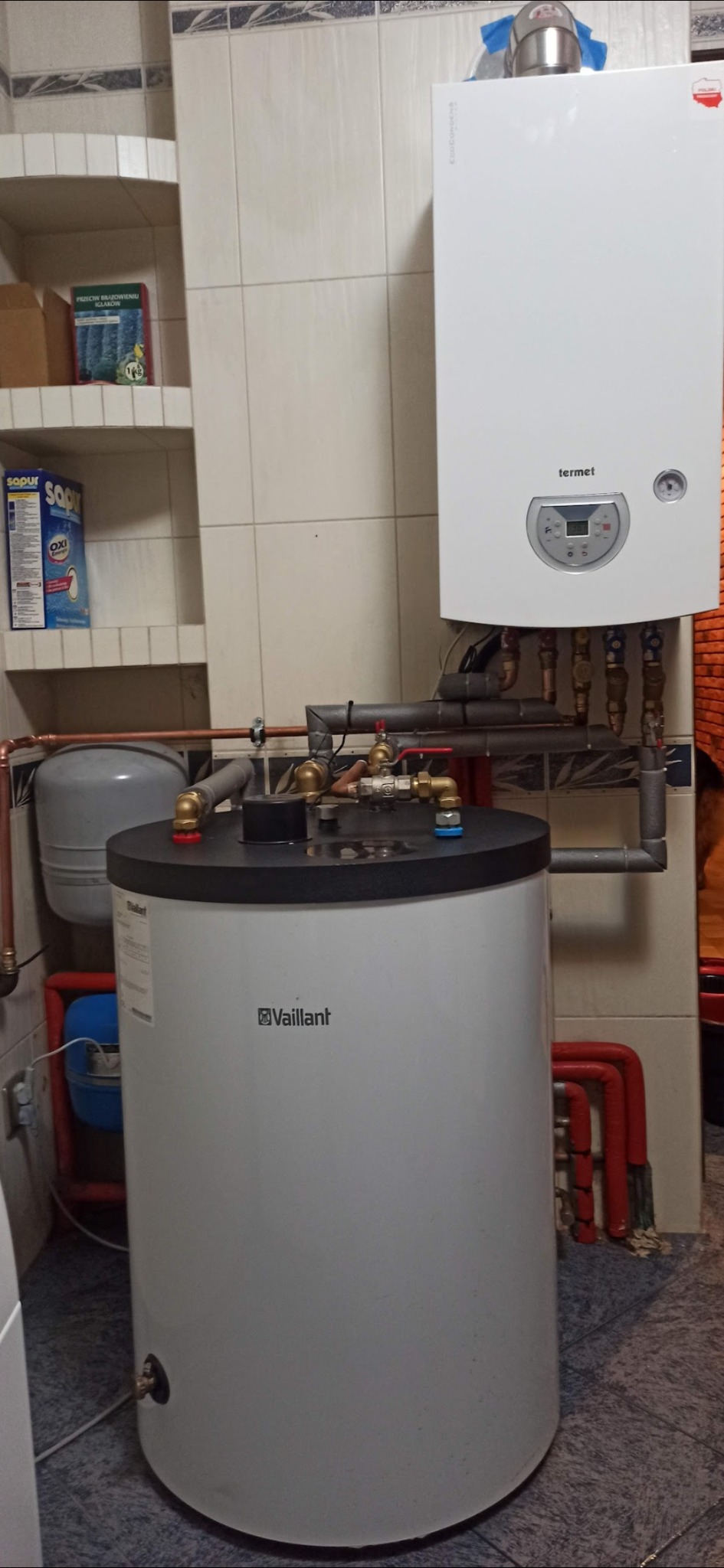Biały piec gazowy Termet i podgrzewacz wody Vaillant z kompletną instalacją hydrauliczną w kotłowni wyłożonej kafelkami.