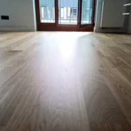 Jasna, odnowiona podłoga drewniana w pokoju z otwartym balkonem, widoczne detale usłojenia drewna i listwy przypodłogowe.