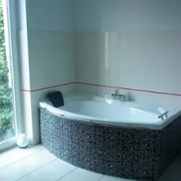 Narożna wanna z hydromasażem, obudowana mozaiką w czarno-białe wzory, z chromowaną armaturą i zagłówkiem, na tle białych płytek z czerwoną listwą, obok okna z widokiem na zieleń.