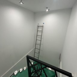 Kolorowy Kąt - Białe ściany po malowaniu w nowoczesnym wnętrzu. Widoczna drabina oparta o ścianę, zabezpieczona podłoga i dekoracyjna balustrada schodów.