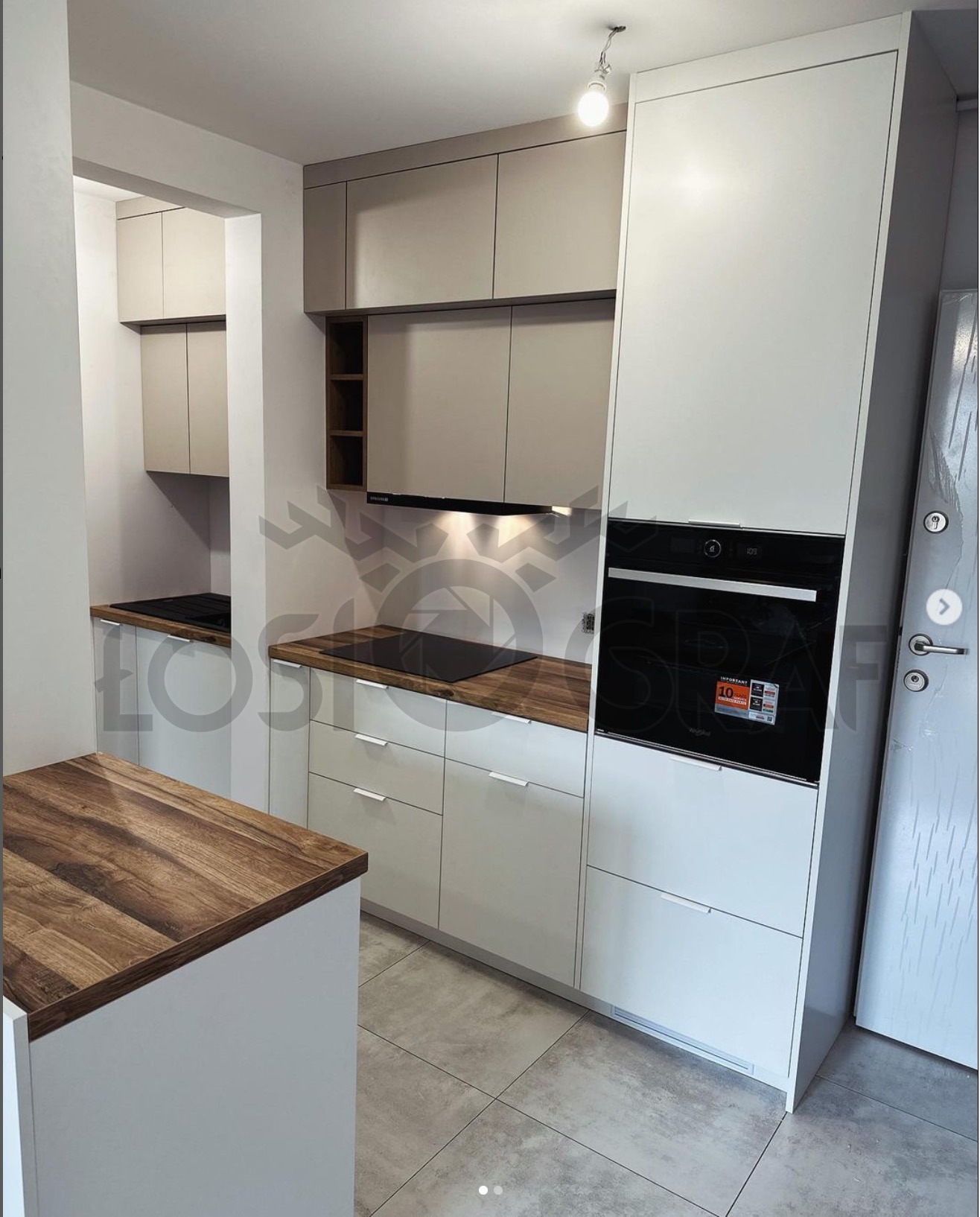 Nowoczesna kuchnia z białymi i beżowymi szafkami, drewnianym blatem i wbudowanym piekarnikiem, widziana z perspektywy wyspy kuchennej.