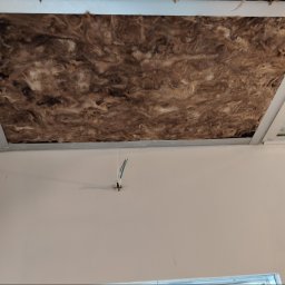 Fijas & Syn - Fragment sufitu podwieszanego z widoczną izolacją z wełny mineralnej i wystającymi przewodami elektrycznymi.