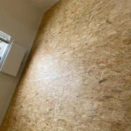 OSB płyty zamontowane na ścianie w nowym budynku, widoczny grzejnik pod oknem i białe ściany.