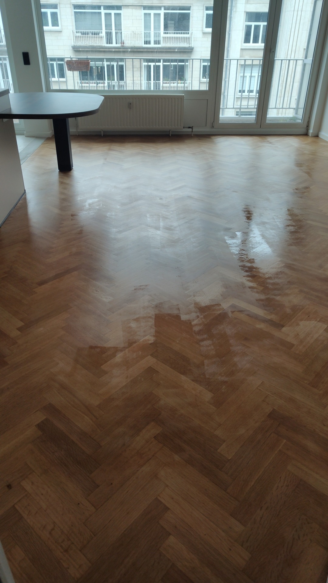 Świeżo polakierowany parkiet ułożony we wzór jodełki francuskiej, odbijający światło z okna balkonowego w mieszkaniu.